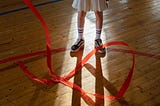 A girl in a gymnasium, twirling an athletic ribbon.