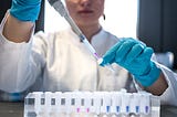 A scientist fills test tubes with a purple liquid. A tray of test tubes with different colored liquids is in front of her.