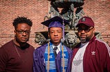 2 young black men and their father. One of the young men is in graduation attire.