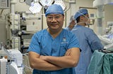 Professor Cheung Tan-To stands in a robotic operating theatreProfessor Cheung Tan-To, dressed in blue scrubs and a blue cap stands in a robotic operating theatre