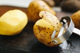 three potatoes with one being peeled with a peeler