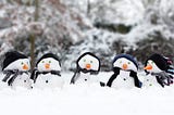 five short snowmen wearing hats and scarfs, all in a row in the snow