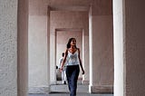 A woman walks away through a shadowed corridor while a man remains behind, symbolizing emotional separation after a breakup.