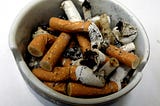 A circular ceramic ashtray that is filled with cigarette ends.