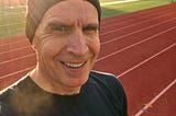 A runner wearing a beanie at a track at sunrise
