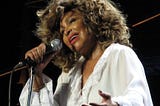 Tina Turner slinging in a white blouse and black pants