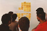 6 pessoas olhando para uma parede com vários post-its