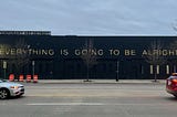 On the side of a building, the words “EVERYTHING IS GOING TO BE ALRIGHT”.