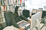 Man wearing a halloween mask and eyeglasses on his office computer