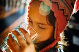 A child in a snow hat drinks a clear glass of water.