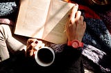 A woman reading a book with a cup of coffee.