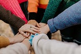 Photo of multiple people placing their hands on top of one another in a gesture of solidarity.