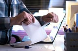 Person sitting in front of laptop tearing paper in half