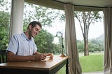 A well-groomed man looking happily at a beautiful pastoral scene from his office window