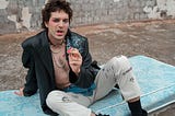 a surly man is dressed as a punk type sitting on an old mattress