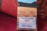 A photograph of the author’s copy of “The Gilded Cage” by Mark Twain propped against a cushion.