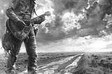 This black and white image presents a striking portrayal of a rugged musician in a cowboy hat, immersed in playing his guitar while standing on a muddy, desolate road. His attire and the worn-out guitar emphasize a life perhaps filled with hardships and stories. The dramatic sky above, teeming with clouds, adds a powerful, almost cinematic quality to the scene, enhancing the sense of a narrative unfolding in this isolated landscape. The composition evokes themes of resilience, solitude, and the