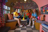 Photo of five queer youth in a colorful room waiving LGBTQ flags