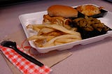 school lunch in a styrofoam tray including a fried chicken sandwich, french fries, and green beans