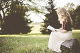 blonde woman reading a book in a field
