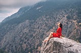 a girl in a red dress on top of a cliff admiring the view of a mountain gorge