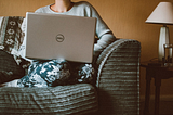 Image of a women sitting on a couch with a computer balanced on her knees