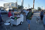 Leo Walhood, in a green jacket and shorts, is featured supporting a local street vendor in Boyle Heights.