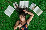 Woman lying in the grass surrounded by books