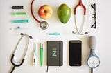 Upper view of a table with stethoscope, mobile, spectacles, pens, syringes, fruits etc on it.