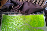 A dark brown wax jacket is piled on a chair, opened out to show that the lining has been patched with a piece of artist’s canvas painted bright green and decorated with a gold tree.