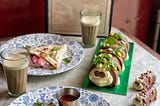 A photograph of a table laid with 2 chais, a colin the caterpillar cake, 2 colin mini cakes and 2 plates with spoof percy pig naan bread wraps and a menu