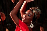 Black dancer with shimmering head wrap, hands in the air head tilted back with large round cream earings