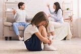 Young child listens as parents argue in background.