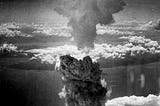 Billowing mushroom cloud rising over Nagasaki on August 9, 1945, captured from the air against a backdrop of scattered clouds.