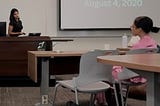 Sarah in black speaking in front of a podium to a class of students.