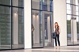 Business woman on phone, red hair, smartly dressed, large handbag, outside a glass fronted building