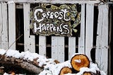 Hand painted sign on a rustic fence saying “Compost happens” above a pile of wood.