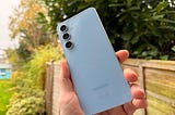 Blue Samsung S24 FE phone. The backdrop is a grassy scene.