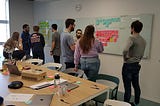 A group of people deliberate over different coloured post-its on a whiteboard in a card-sorting activity