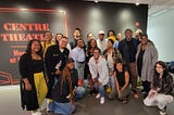 A diverse group of Groundwork Regional Lab participants posed in front of a black wall with words “Centre Theatre” printed on it in orange letters.
