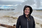 Jackie standing in black zipped hoodie in front of geyser.