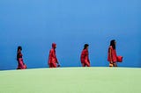 Five models in red walk against the blue background of the fashion show.