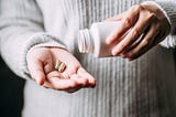 woman holding pill bottle in one hand and two capsules of medicine in the other