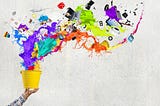 A person holding a bucket that has colored paint and items spilling out of it