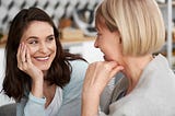 Two women of different ages smile and chat together warmly.