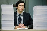 Still from the movie ‘The Report’ shows Dan Jones, played by Adam Driver, a Senatorial investigator at his desk in front of 2 towers of paper.