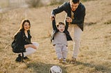 Wife watching father playing soccer with his young son