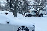 Winter street scene with people walking, snowplow, and a snow covered car