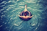 Man floating in an inner tube on a calm lake on a sunny day.
