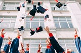 Group of fresh graduates students throwing their academic hats in the air in front of a building.